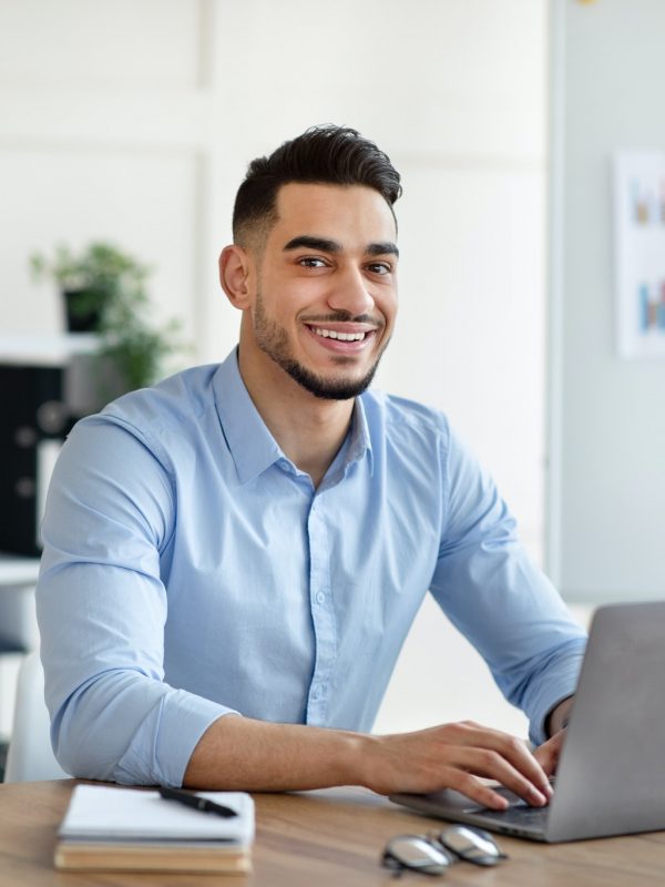 Attractive young Arab businessman using laptop pc at his desk in home office Attractive young Arab businessman using laptop pc at his desk in home office